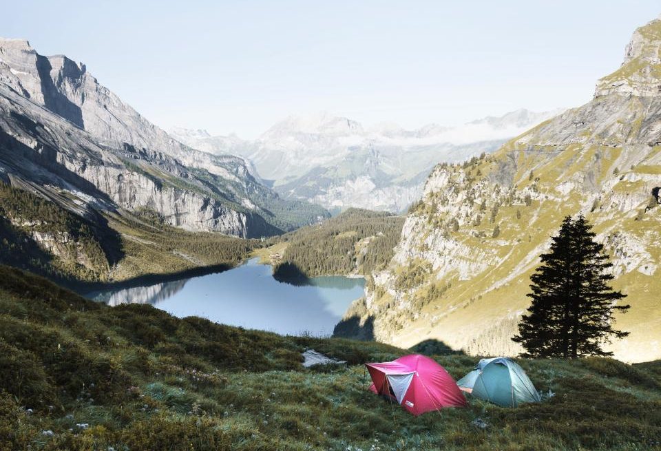 Two small tents on a grassy slope high above a mountain lake