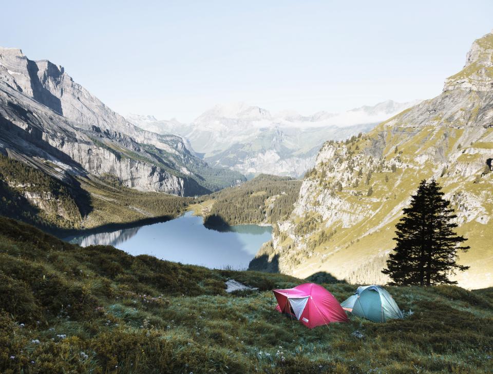 Two small tents on a grassy slope high above a mountain lake